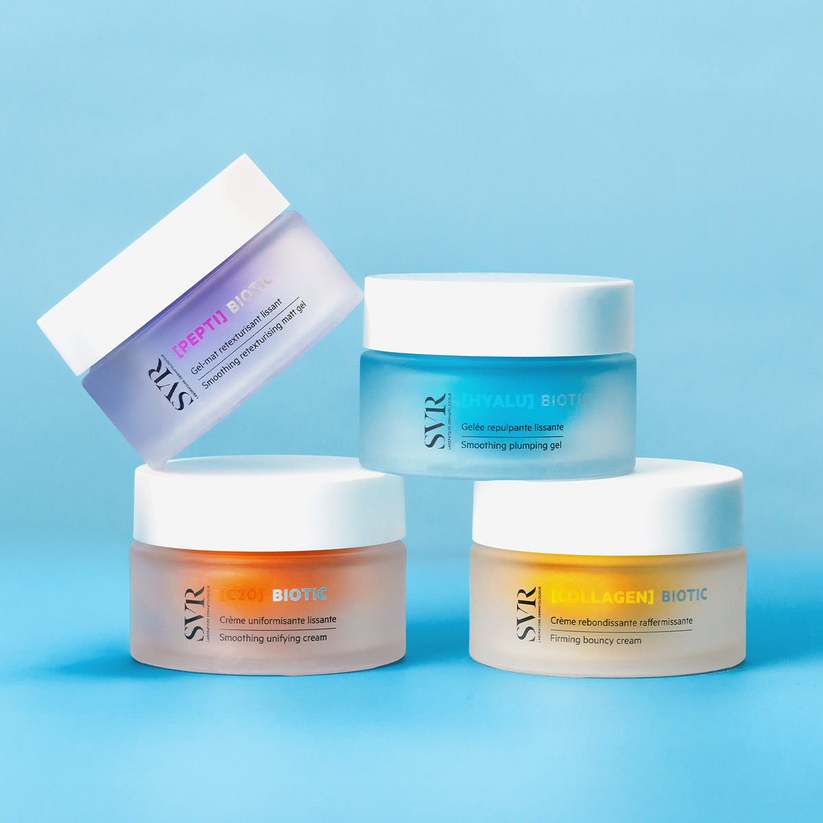 Quatre pots de crème SVR Biotic aux couleurs pastel et couvercles blancs, disposés sur un fond bleu clair.