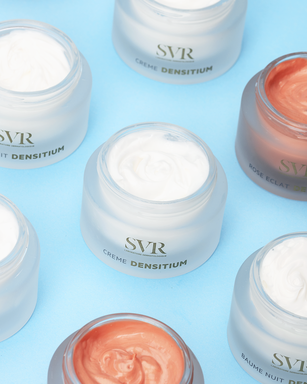 Pots de crème SVR Densitium aux textures blanches et rosées disposés sur un fond bleu clair.