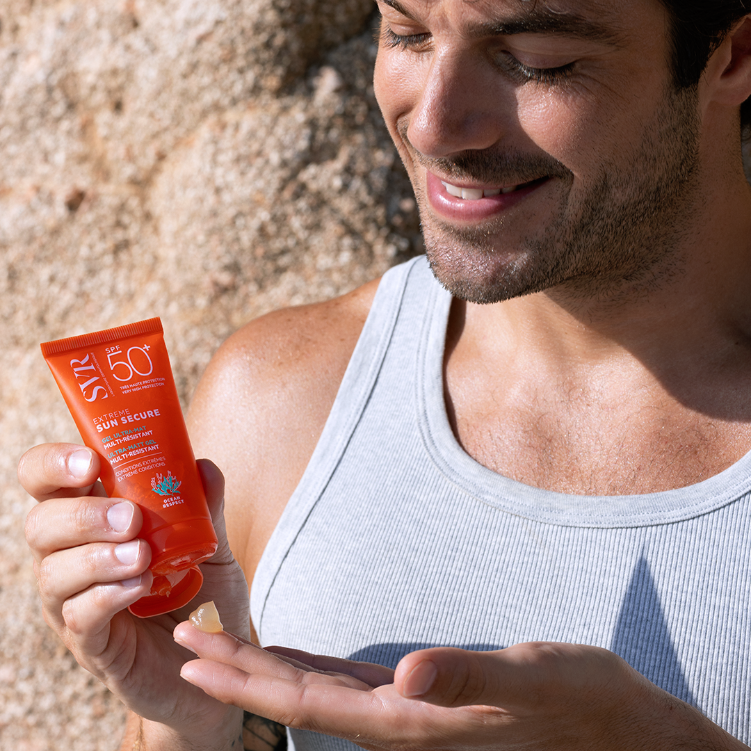 Homme en débardeur gris appliquant le gel solaire SVR Sun Secure SPF 50+ orange sur sa main en extérieur.