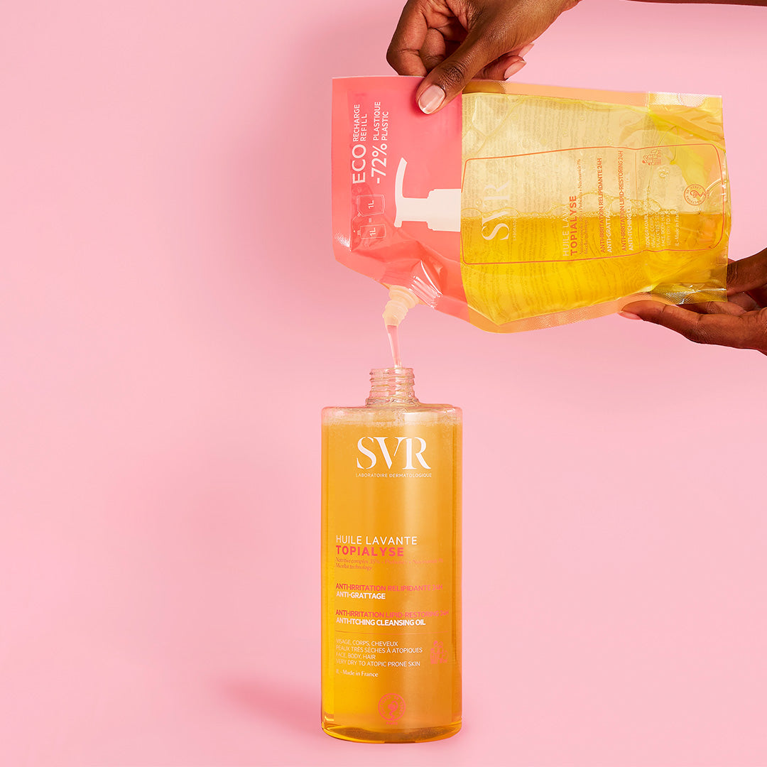 Recharge éco SVR Topialyse Huile Lavante 1L versée dans un flacon pompe transparent sur fond rose.