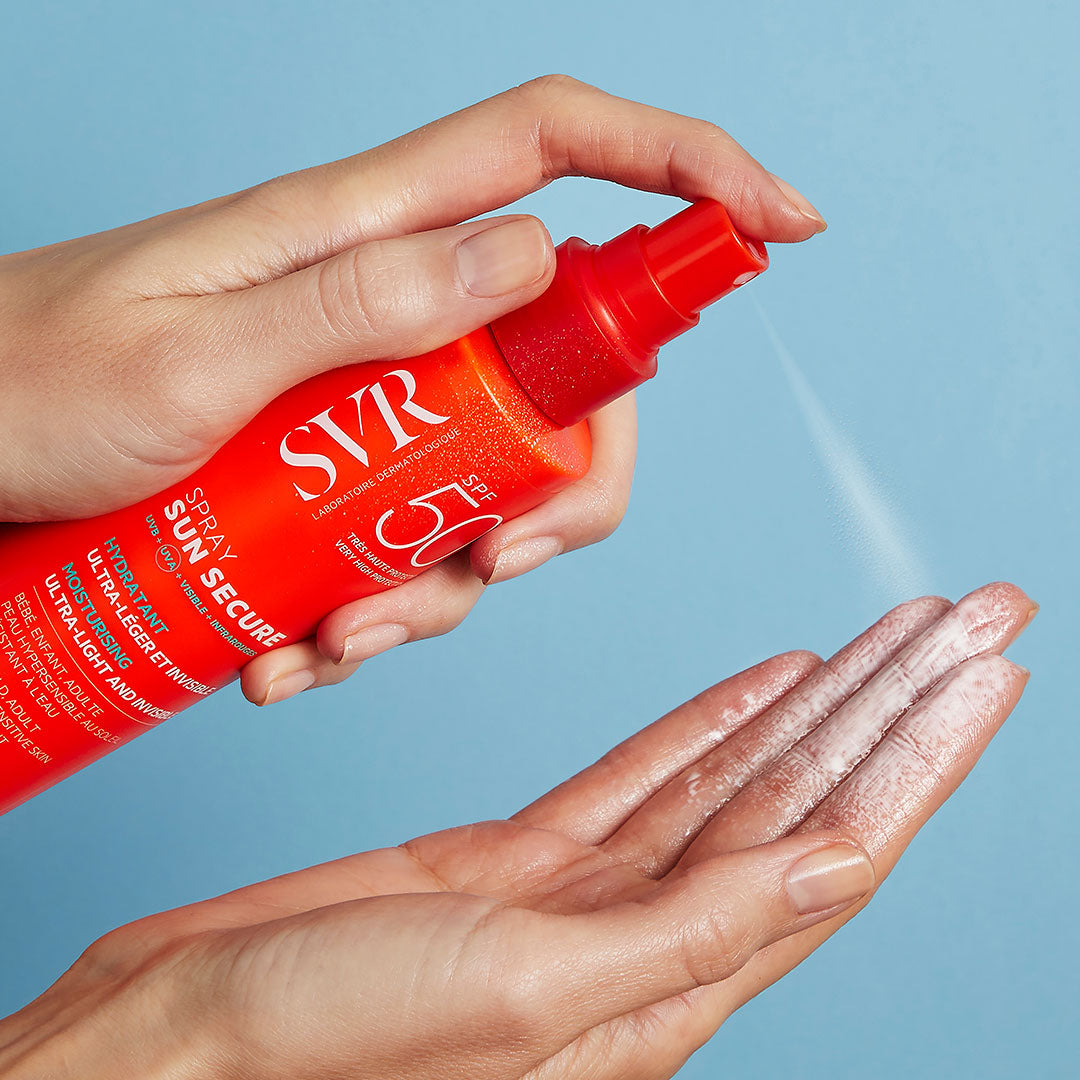 Main pulvérisant le spray solaire SVR SUN SECURE SPF50+ orange sur une paume ouverte sur fond bleu.