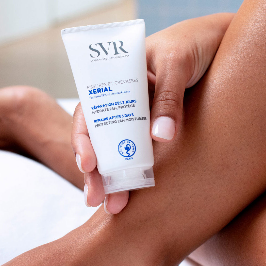 Tube blanc de crème SVR Xerial Fissures et Crevasses tenu en main par une femme, avec texte bleu sur fond blanc.