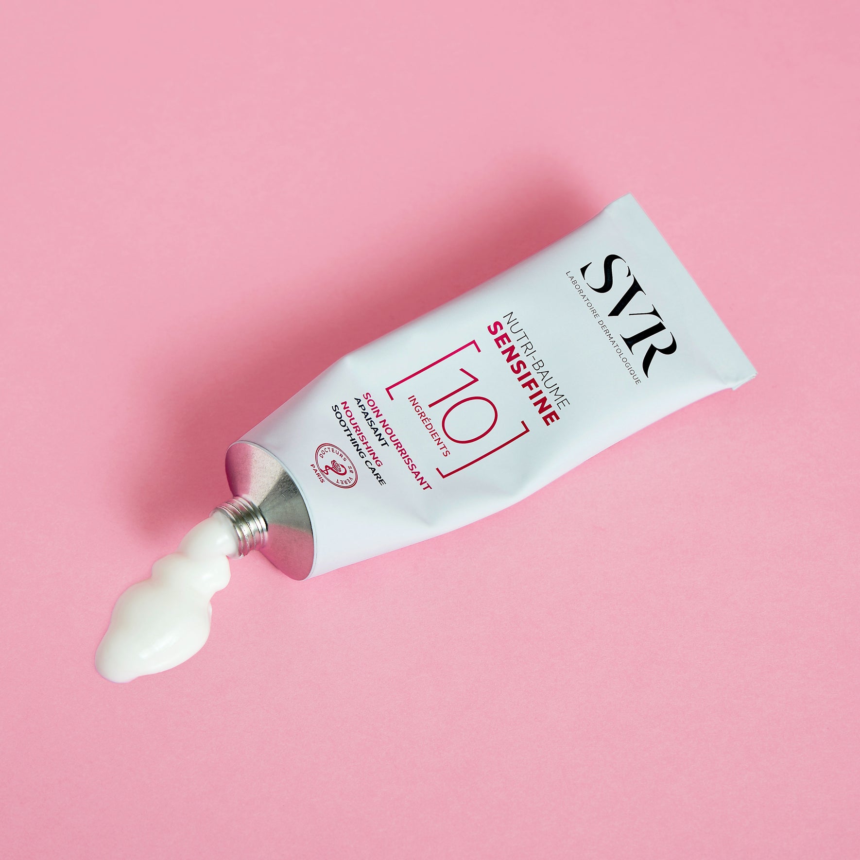 Tube en aluminium SVR Sensifine Nutri-Baume avec texture crème blanche sur fond rose, soulignant sa formule minimaliste.