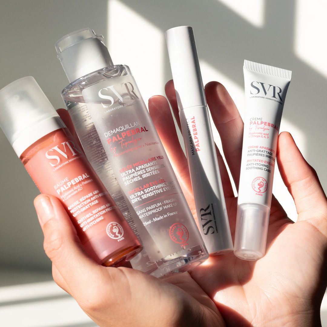 Main tenue tenant quatre produits SVR Palpebral : un baume rose, un démaquillant transparent, un mascara et une crème apaisante.