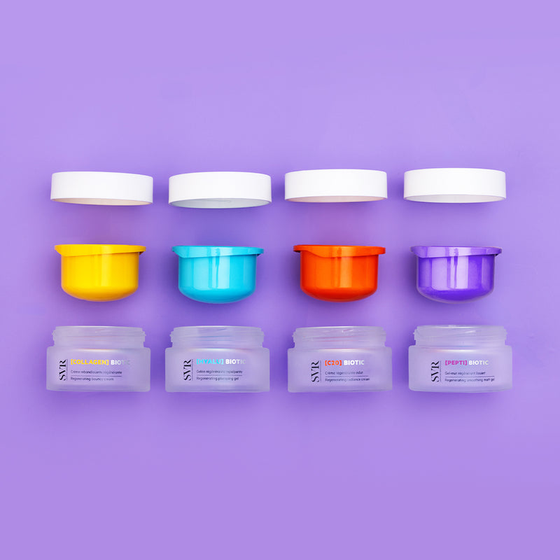 Quatre pots de crème SVR Biotic avec couvercles blancs et opercules colorés jaune, bleu, orange et violet sur fond lilas.