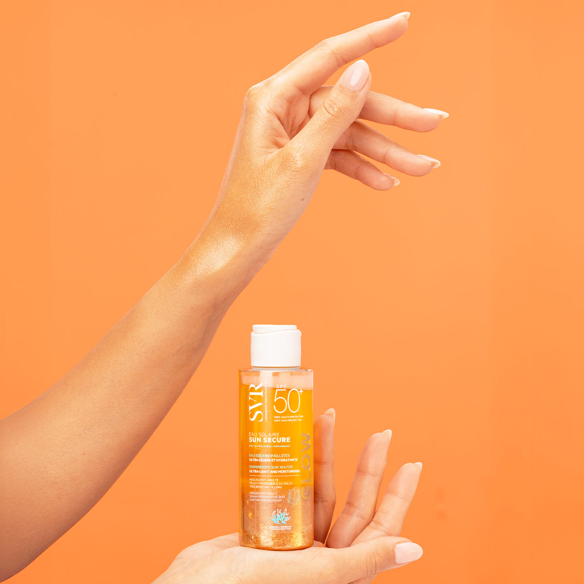 SVR SUN SECURE SPF50+ shimmering sun water bottle held by a hand against an orange background.