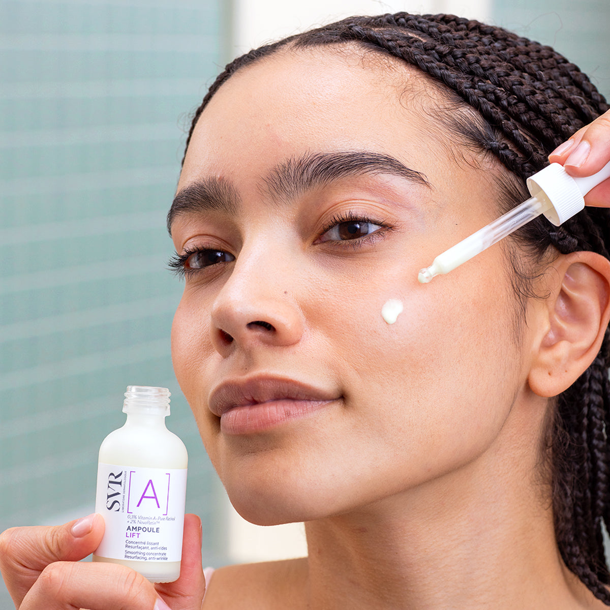 Femme appliquant le sérum SVR Ampoule Lift avec une pipette sur sa joue, flacon en verre blanc avec étiquette violette.