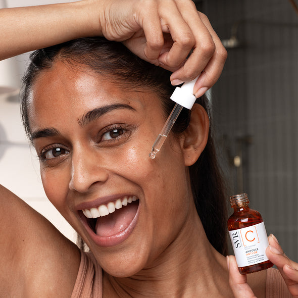 Femme souriante appliquant le sérum SVR Ampoule Anti-Ox avec une pipette sur son visage, flacon en verre ambré en main.