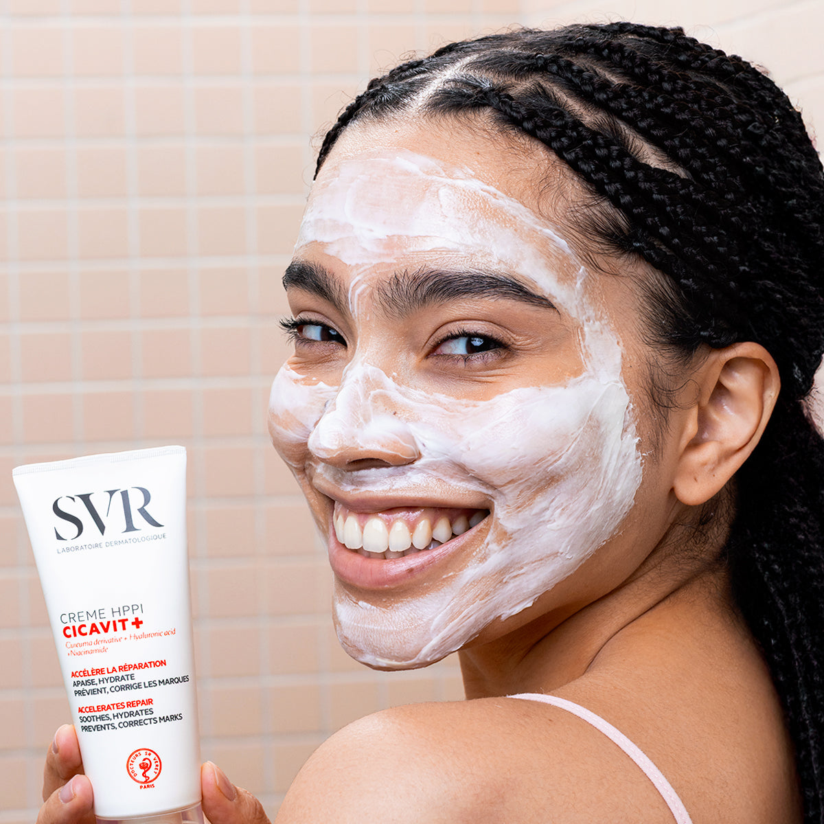 Femme souriante appliquant la crème réparatrice SVR Cicavit+ HPPI sur son visage avec une texture blanche effet pansement.