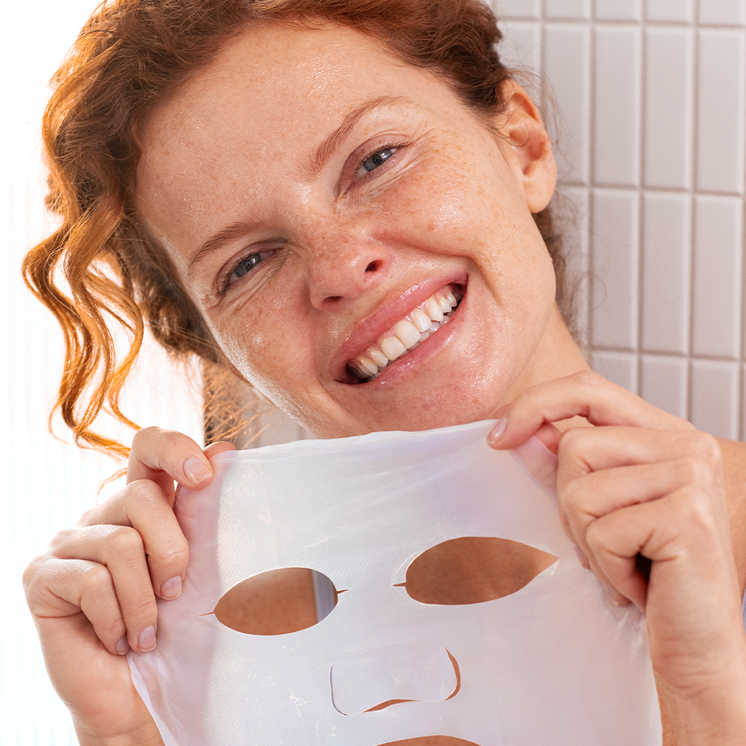 Femme souriante tenant un masque en biocellulose blanche hydratant B3 pour le soin du visage.