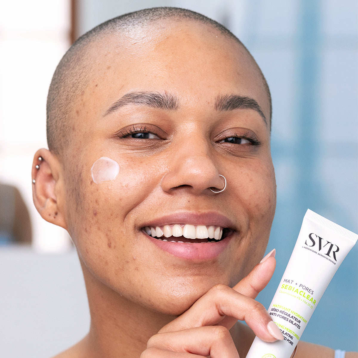 Personne souriante appliquant la crème matifiante SVR Sebiaclear Mat+Pores sur sa joue pour réduire les pores et le sébum.