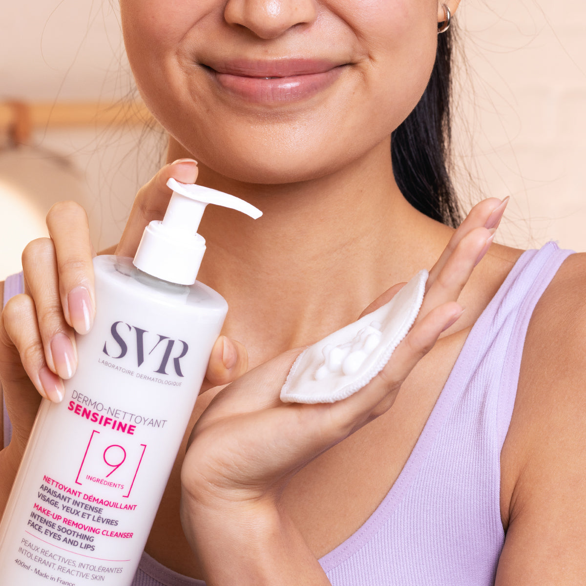Flacon pompe SVR Sensifine Dermo-Nettoyant 400ml avec texture gel crème sur un coton, tenu par une femme souriante.