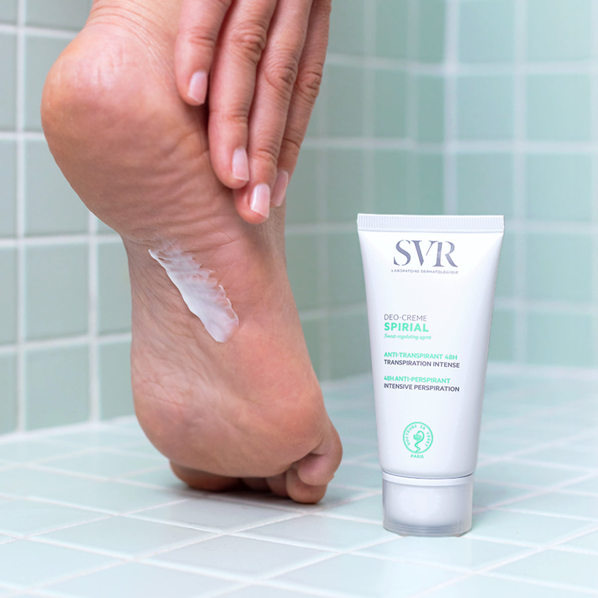 Tube de crème anti-transpirante SVR Spirial blanc posé sur un carrelage vert près d'un pied recevant une application de soin.