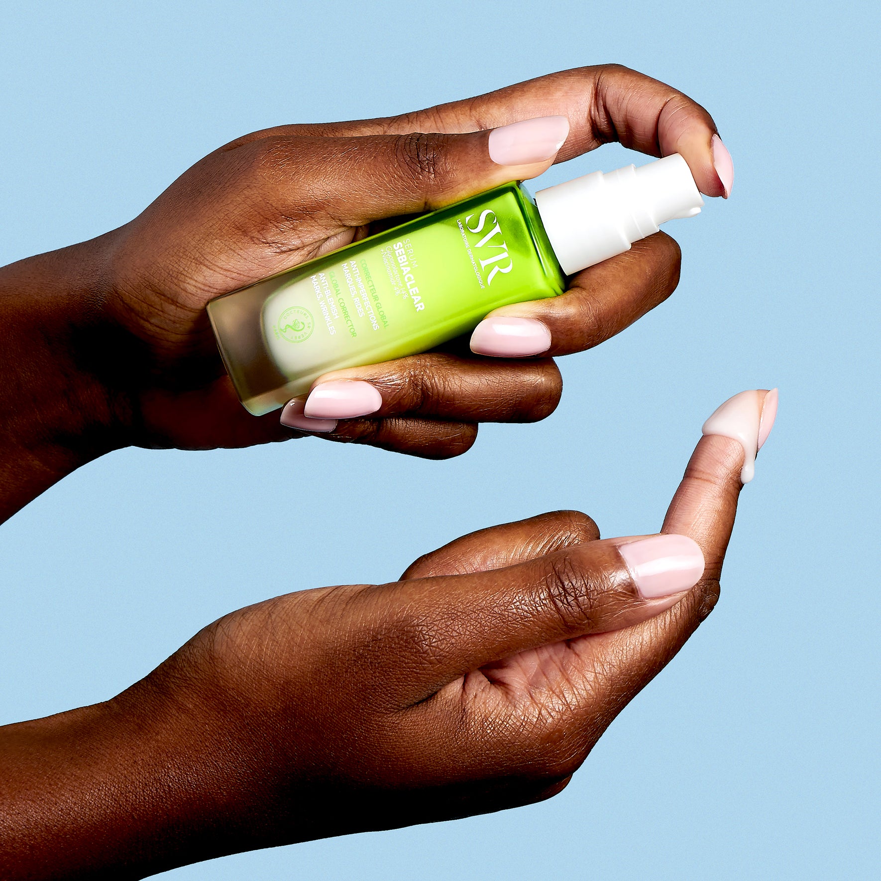 Hands holding a green SVR Sebiaclear serum bottle with a white pump, dispensing a drop of white cream onto a fingertip.