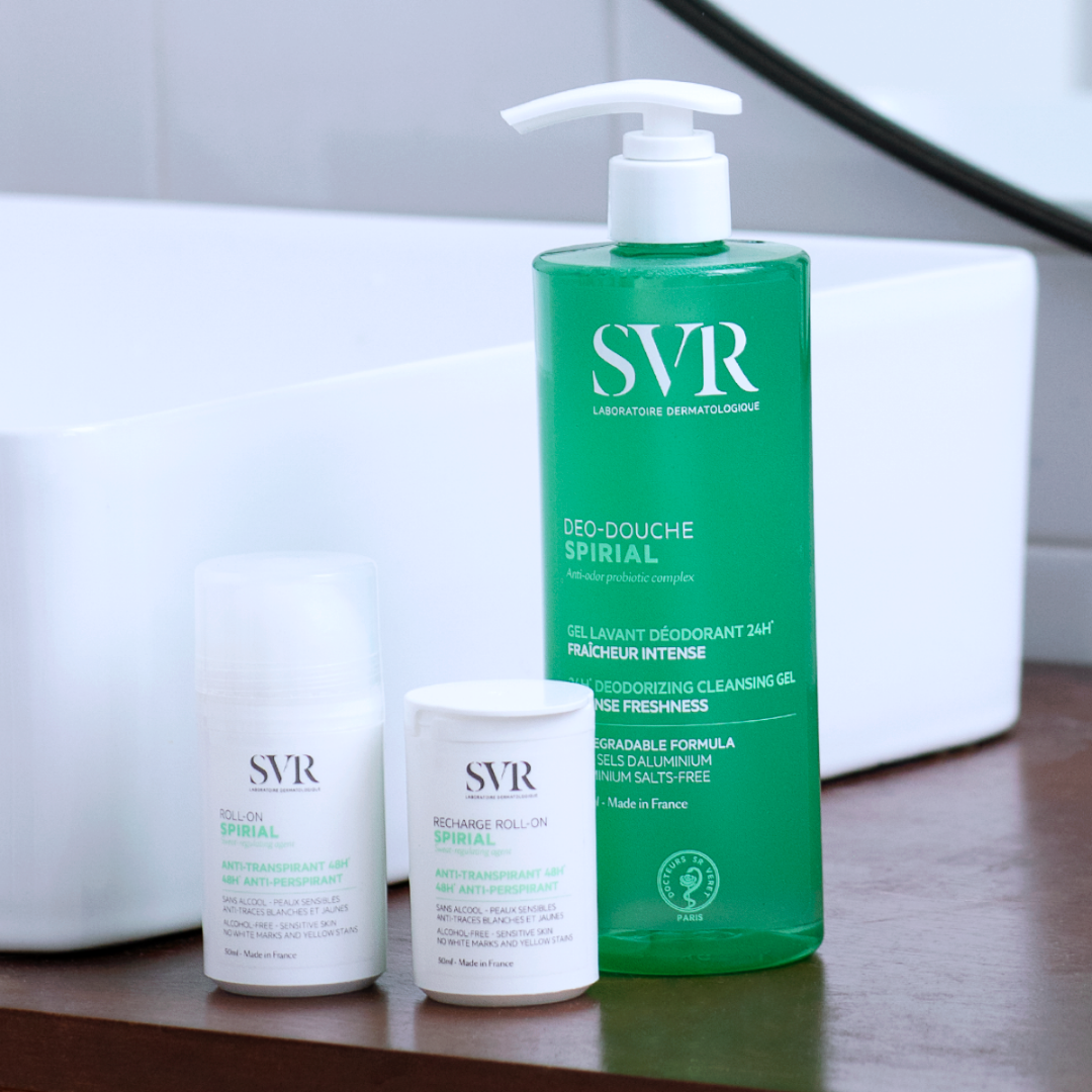 Gel douche SVR Spirial vert à pompe et deux déodorants roll-on blancs sur un rebord de lavabo.