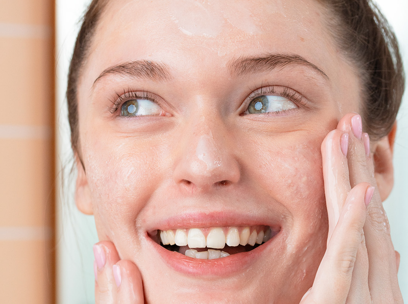 Jeune femme souriante appliquant un soin nettoyant sur son visage pour traiter les imperfections de la peau.