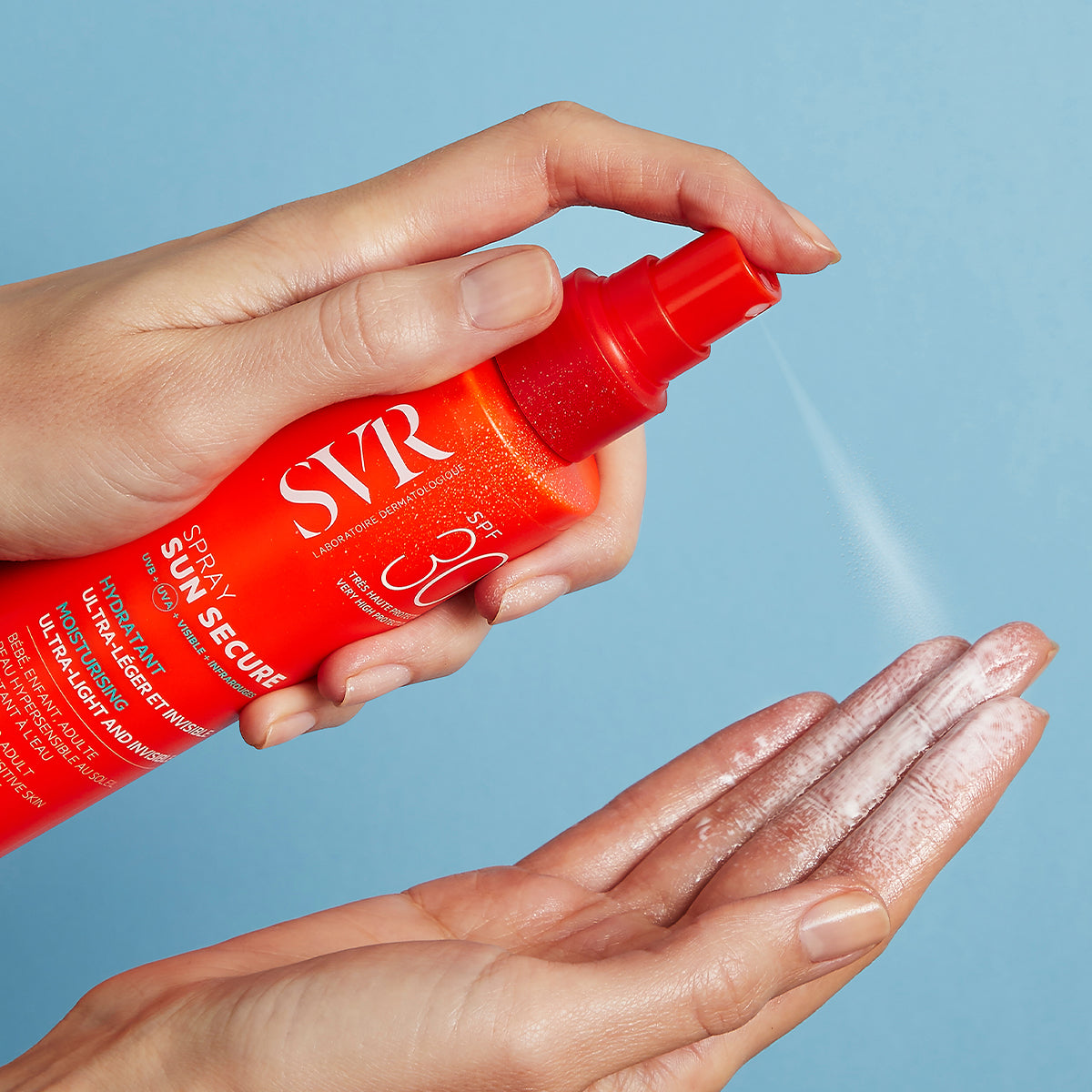 Main orange SVR SUN SECURE SPF30 spray vaporisant une brume solaire légère sur une main sur fond bleu.