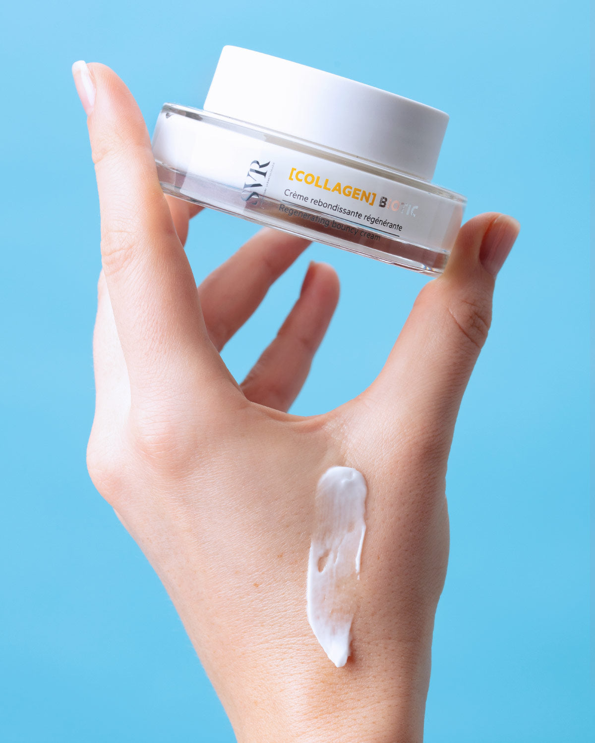 Main tenant un pot de crème SVR Collagen Biotic blanc et transparent avec une texture onctueuse appliquée sur la main.
