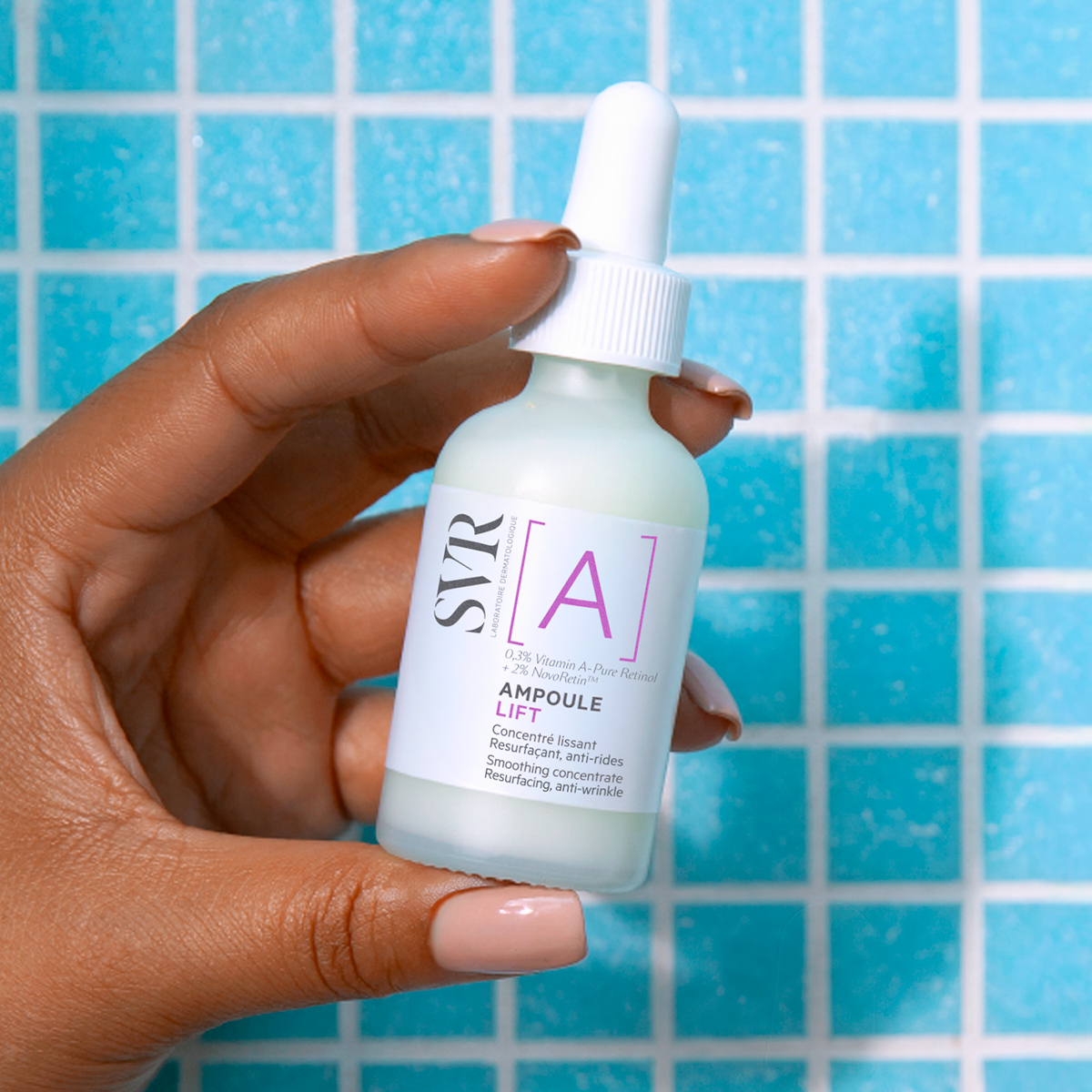 Main tenue en main d'un flacon compte-gouttes SVR [A] Ampoule Lift sur fond de carrelage bleu.