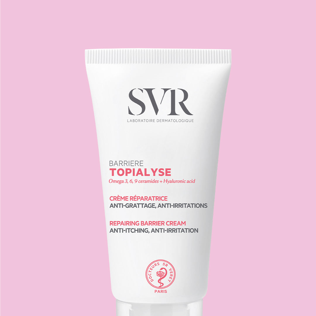 Tube blanc de crème réparatrice SVR Topialyse Barrière sur fond rose, avec texte informatif en noir et rose.