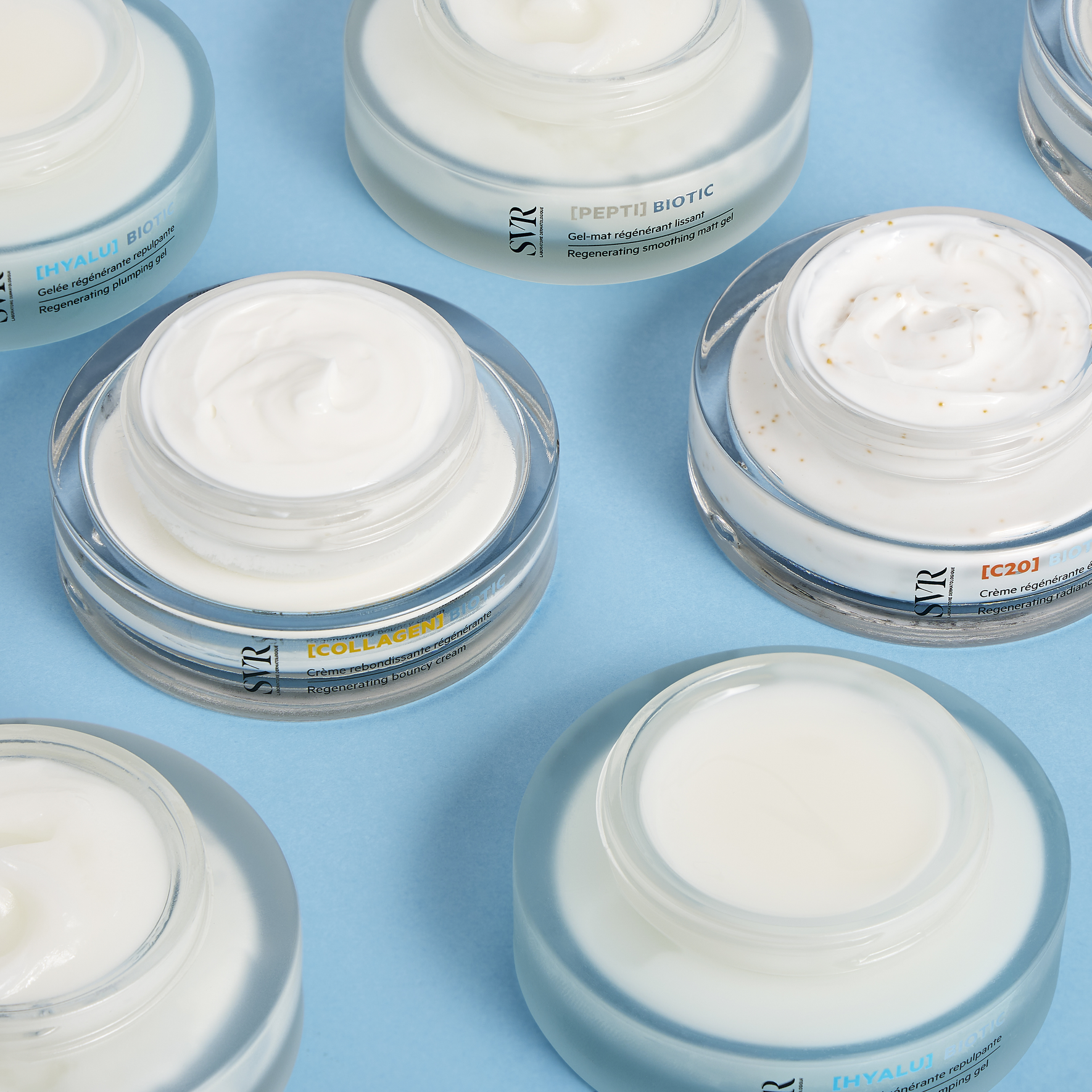 Pots de crème SVR Biotic ouverts sur fond bleu, révélant des textures onctueuses et le pot Collagen Biotic au centre.