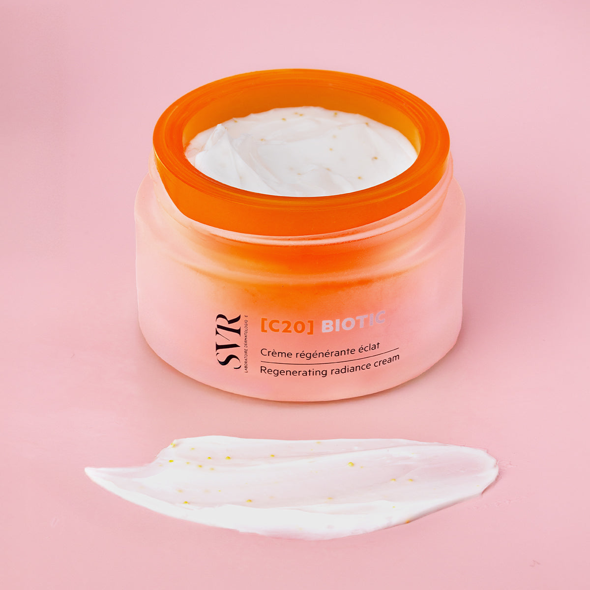 Pot de crème SVR [C20] Biotic en verre dépoli orange avec texture onctueuse et microbilles sur fond rose.