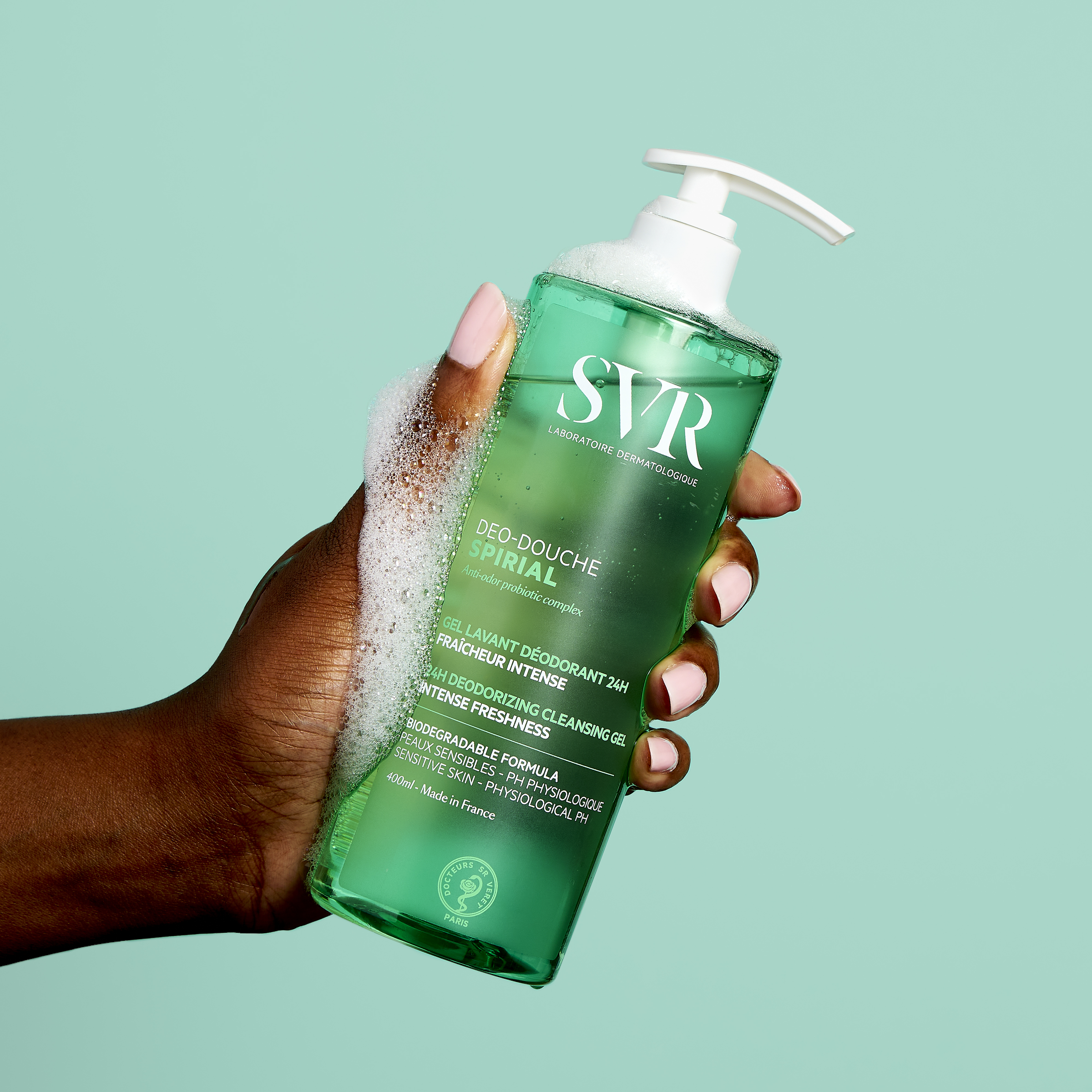 Main tenue par une main, flacon pompe de gel douche SVR Spirial vert translucide de 400ml avec de la mousse sur le dessus.
