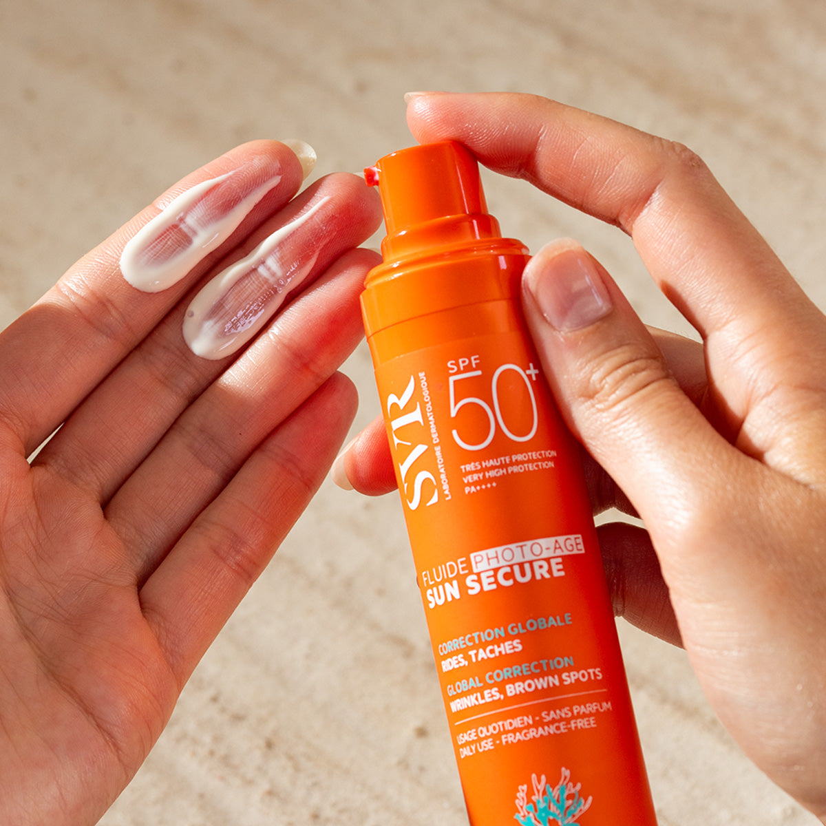 Flacon pompe orange SVR Sun Secure Fluide Photo-Age SPF50+ avec une texture crème légère appliquée sur la paume de la main.