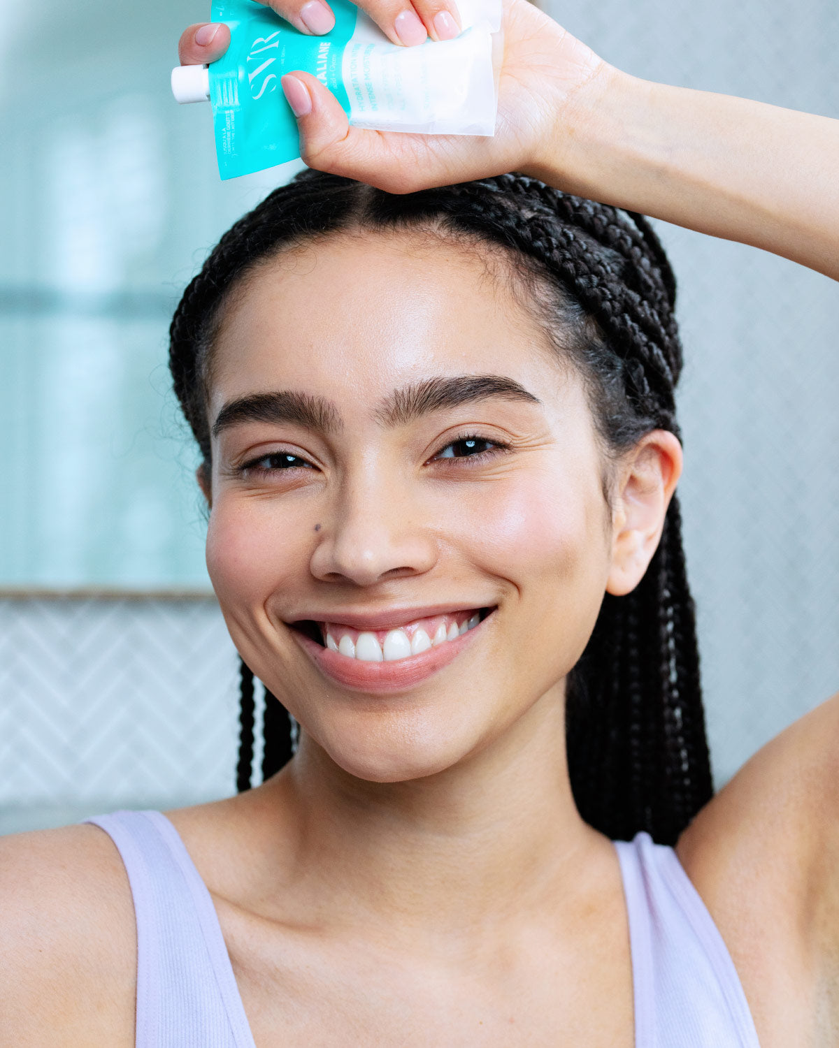 Femme souriante tenant un tube éco-responsable turquoise de crème hydratante SVR Hydraliane près de son visage.