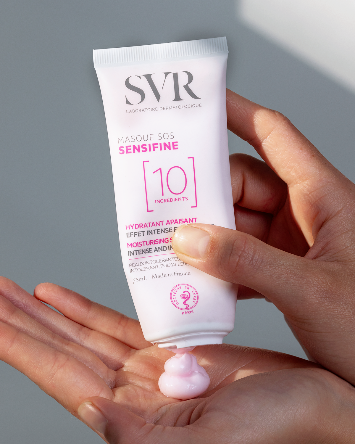 Tube de masque SVR Sensifine SOS rose de 75ml pressé dans une main, révélant une texture crème apaisante de couleur rose.