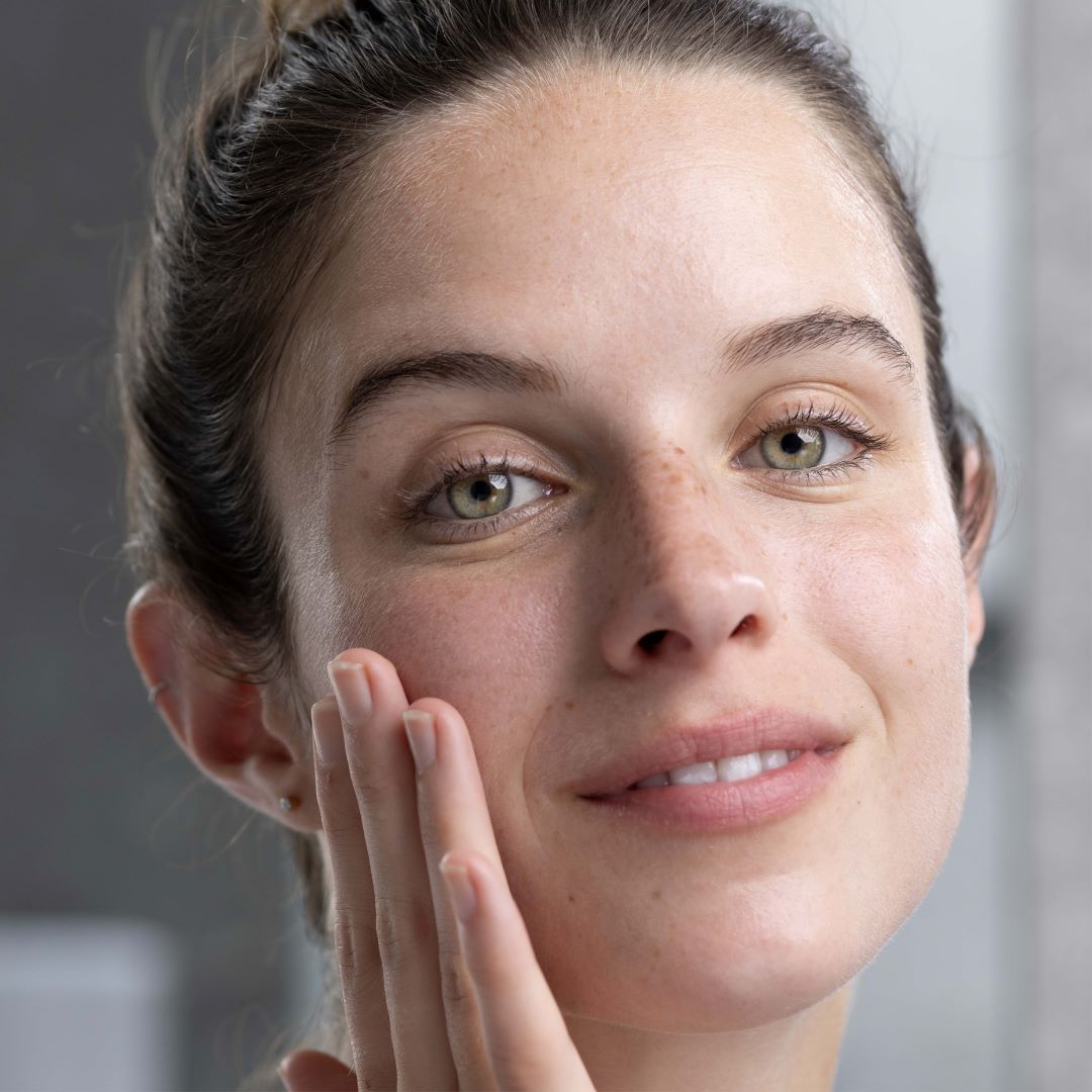 Jeune femme au teint naturel et aux yeux verts appliquant délicatement le gel nettoyant SENSIFINE sur son visage.