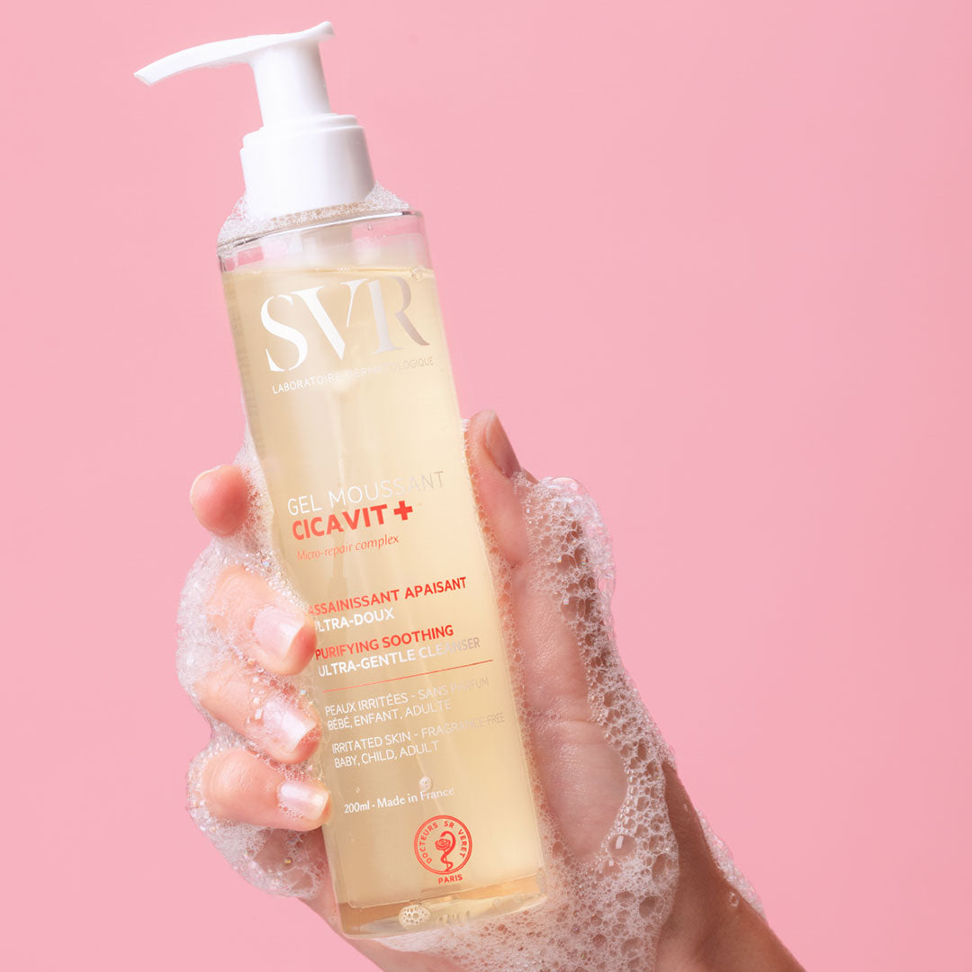 Flacon pompe de gel moussant SVR Cicavit+ 200ml tenu en main avec de la mousse sur fond rose.