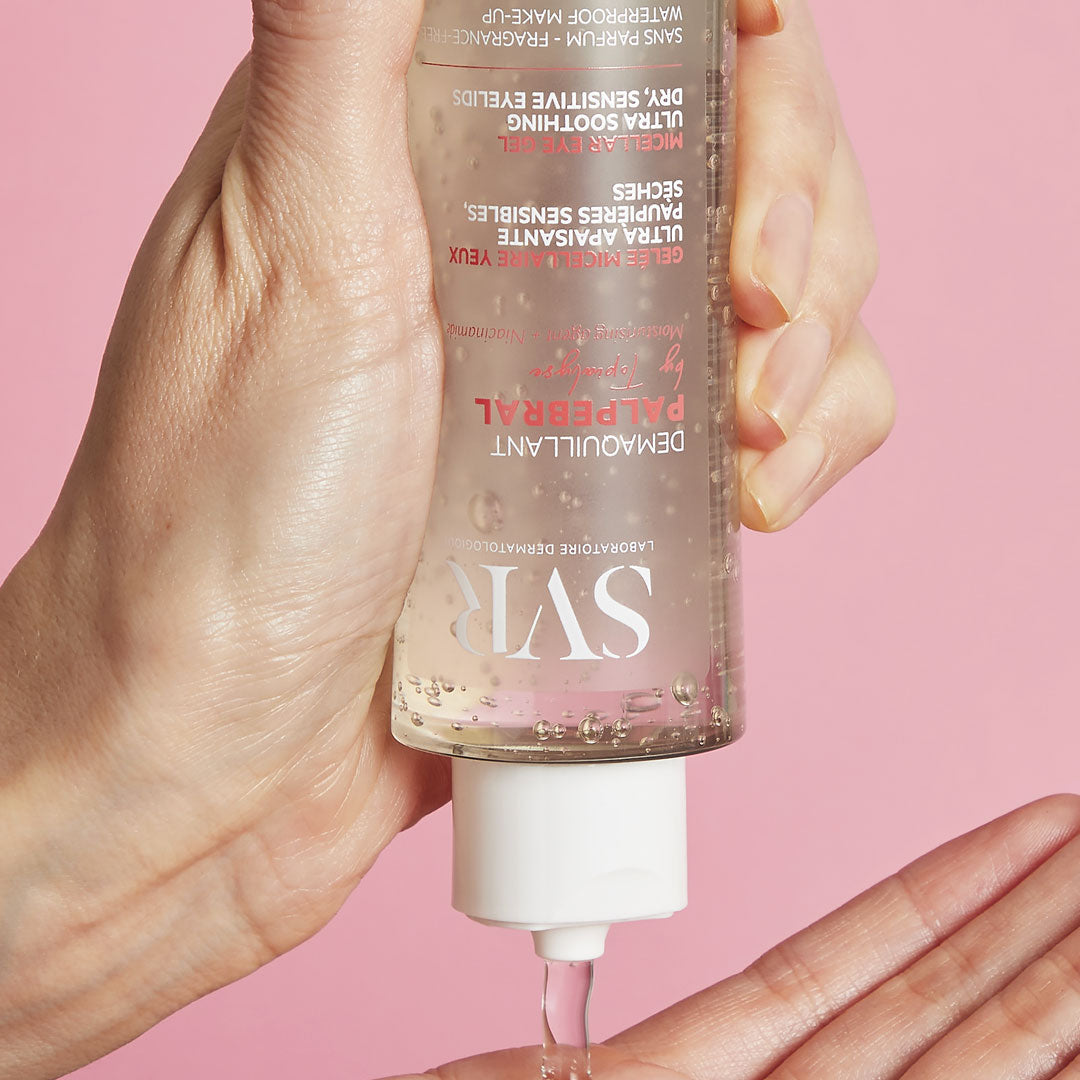Flacon transparent de gel démaquillant SVR Palpebral versé dans une main sur fond rose.