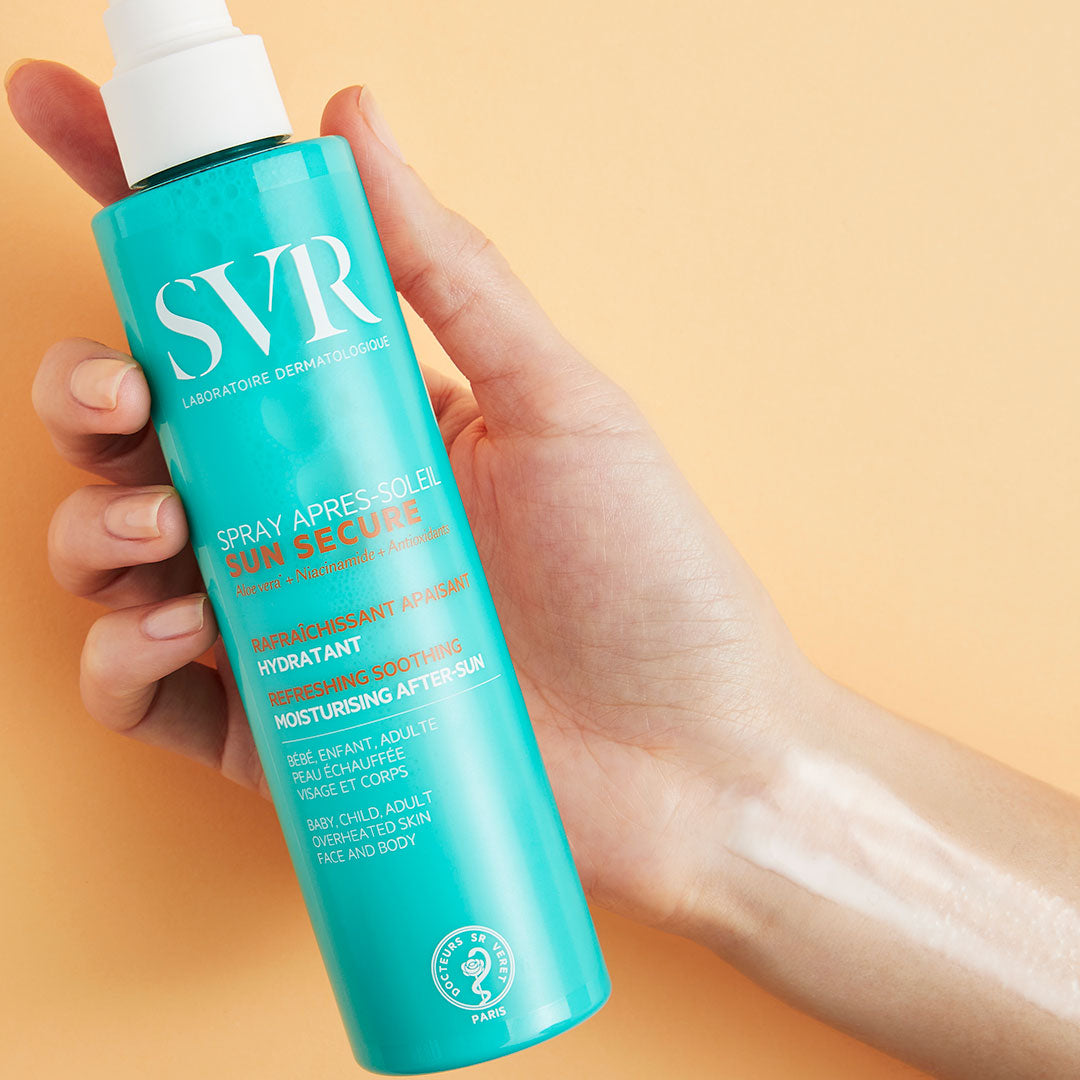 Spray SVR SUN SECURE turquoise tenu en main, avec une brume hydratante appliquée sur le bras sur fond beige.