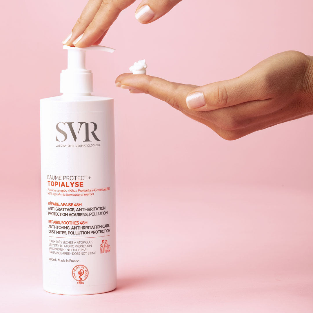 Flacon pompe blanc SVR Topialyse Baume Protect+ avec une noisette de crème onctueuse déposée sur une main, fond rose.