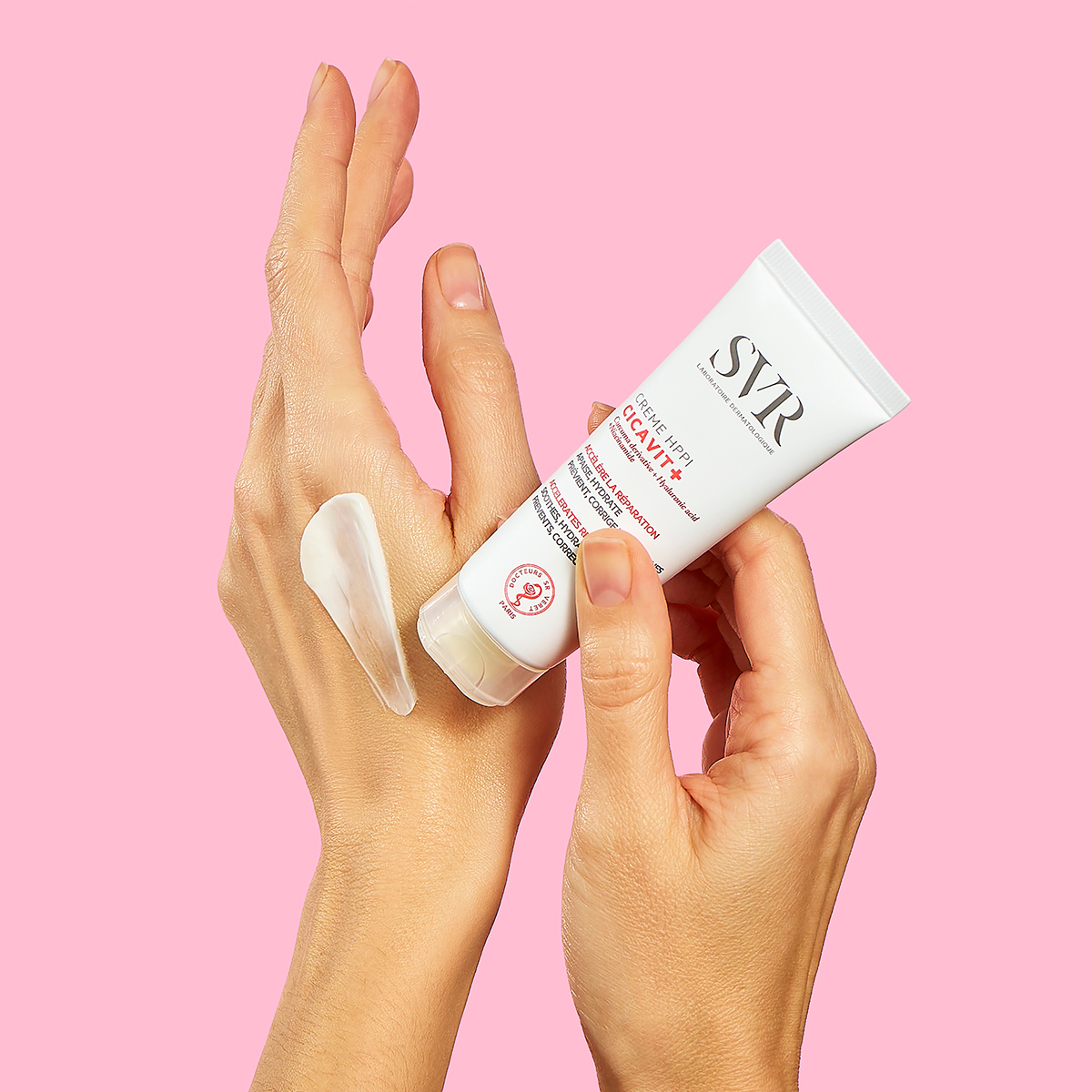 Tube de crème réparatrice SVR Cicavit+ HPPI appliqué sur le dos d'une main sur fond rose.