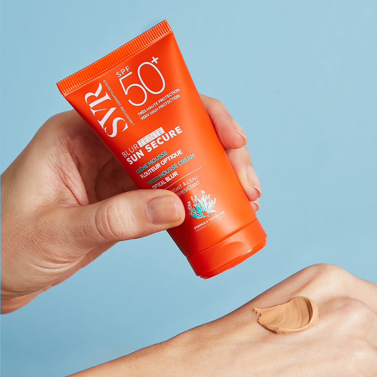 Tube orange SVR Sun Secure Blur teinté SPF50+ appliqué sur la main pour montrer sa texture mousse teintée et veloutée.
