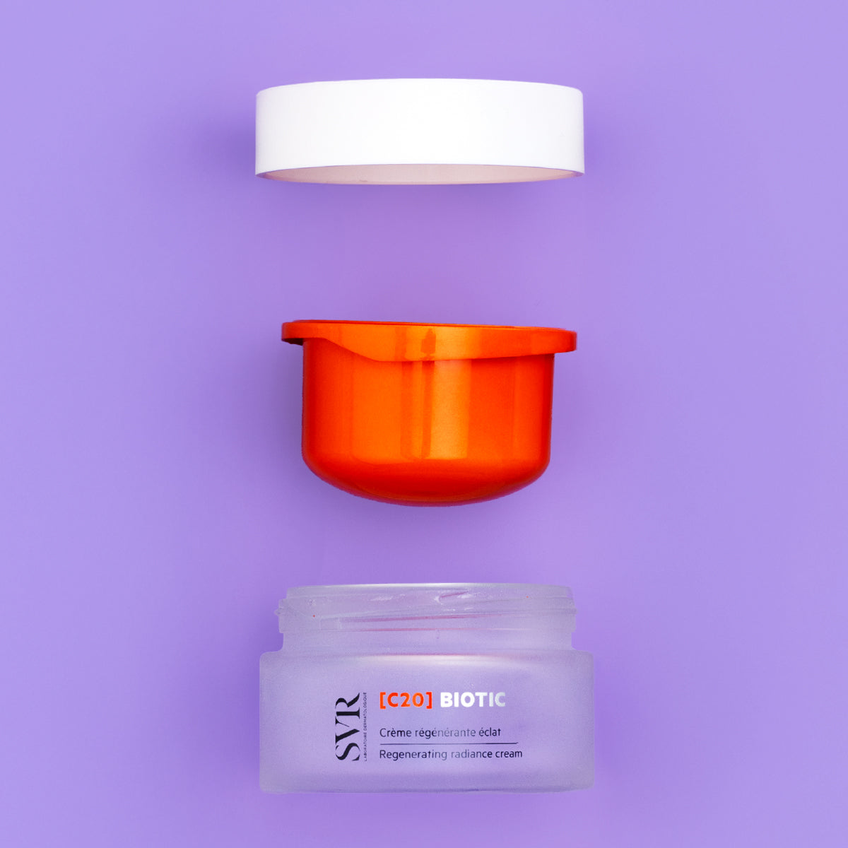 Pot de crème SVR [C20] Biotic avec couvercle blanc, insert orange et base en verre dépoli sur fond violet.