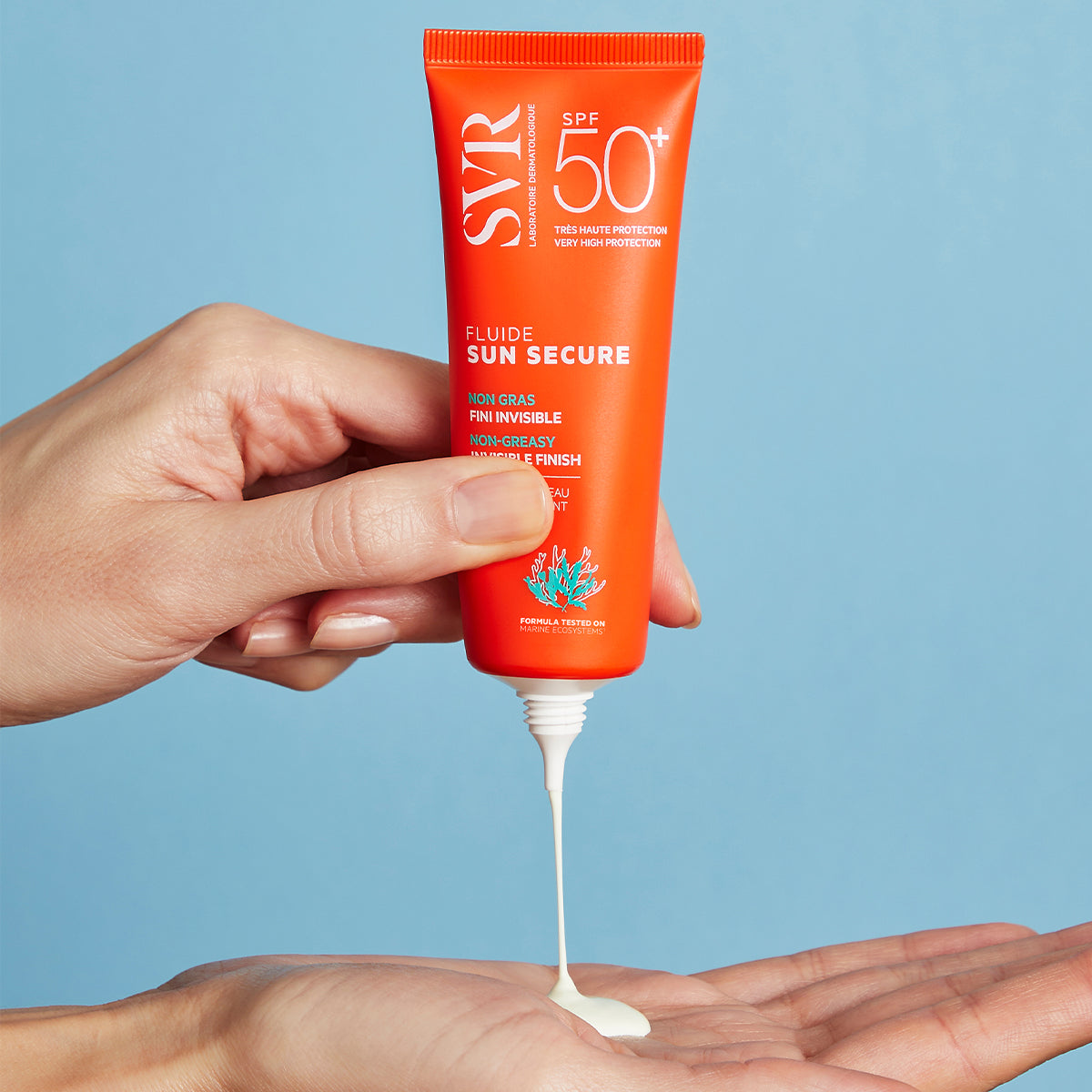 Main orange SVR SUN SECURE SPF50+ fluid tube dispensing white sunscreen onto a hand against a blue background.