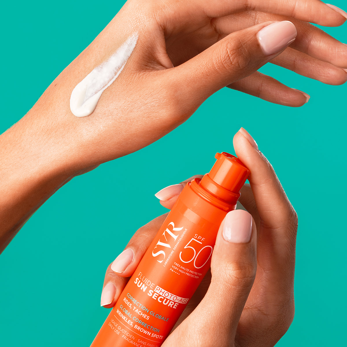 Flacon orange de SVR Sun Secure Fluide Photo-Age SPF50+ tenu en main avec une texture crème blanche appliquée sur la peau.