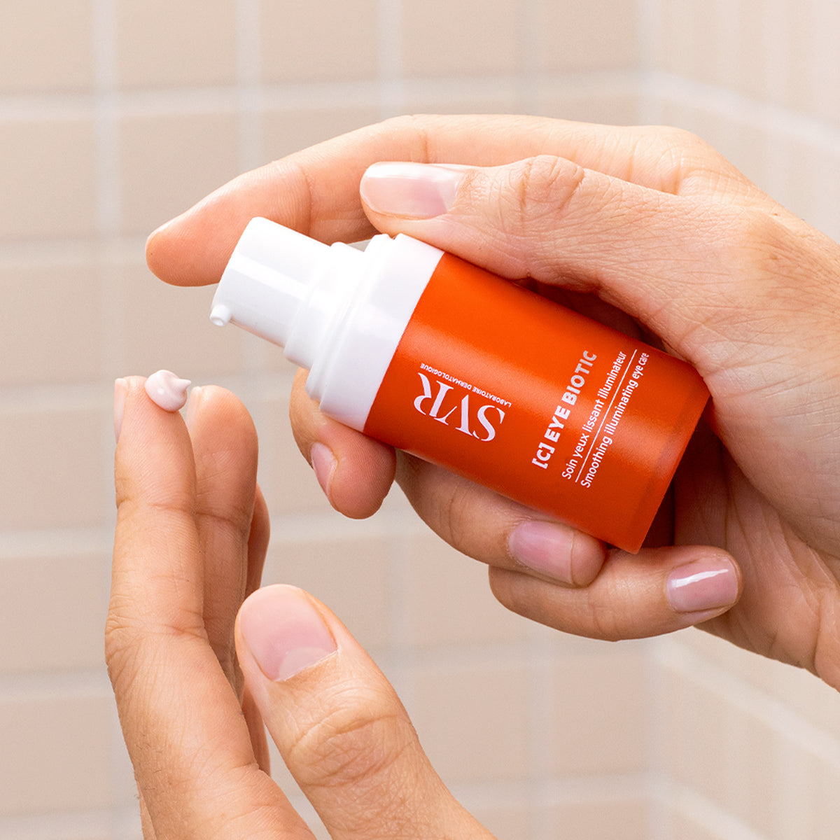 Flacon pompe orange SVR [C] EYE BIOTIC délivrant une noisette de crème lissante sur le bout d'un doigt.