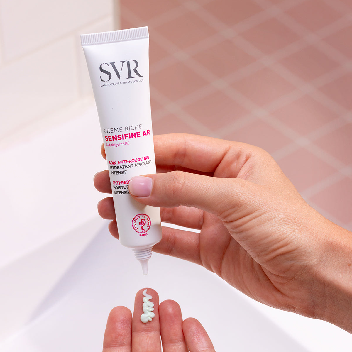 Hand squeezing white SVR Sensifine AR Crème Riche tube, dispensing a dollop of soothing green cream onto fingertips.