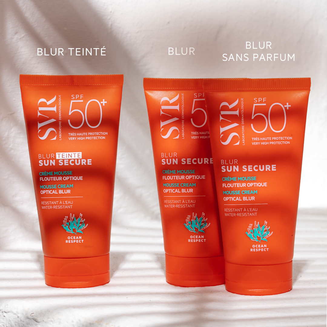Trois tubes de crème solaire SVR Sun Secure SPF50+ orange sur fond blanc avec des ombres de feuilles.