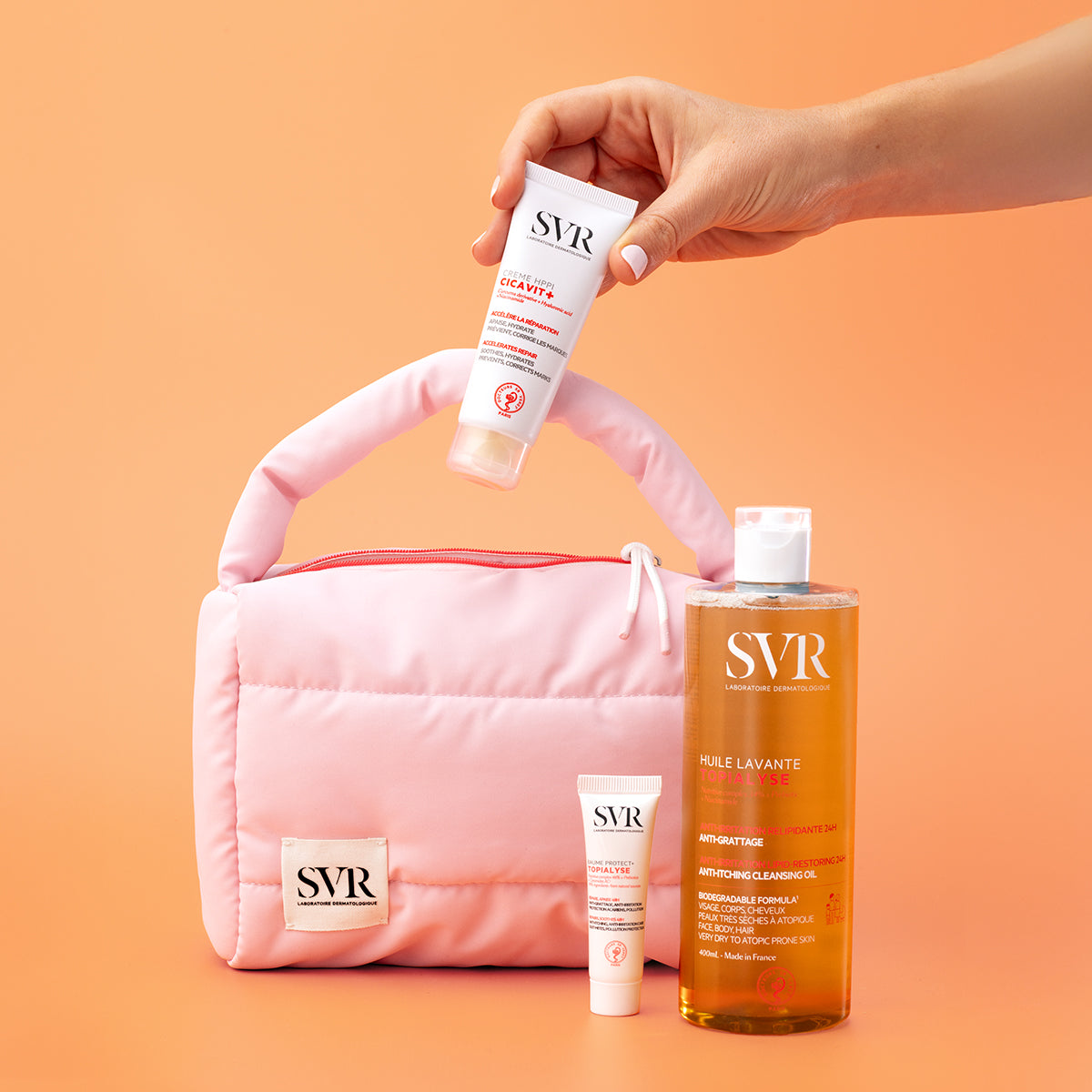 Trousse maternité rose matelassée avec soins SVR Cicavit+ et Topialyse sur fond orange.