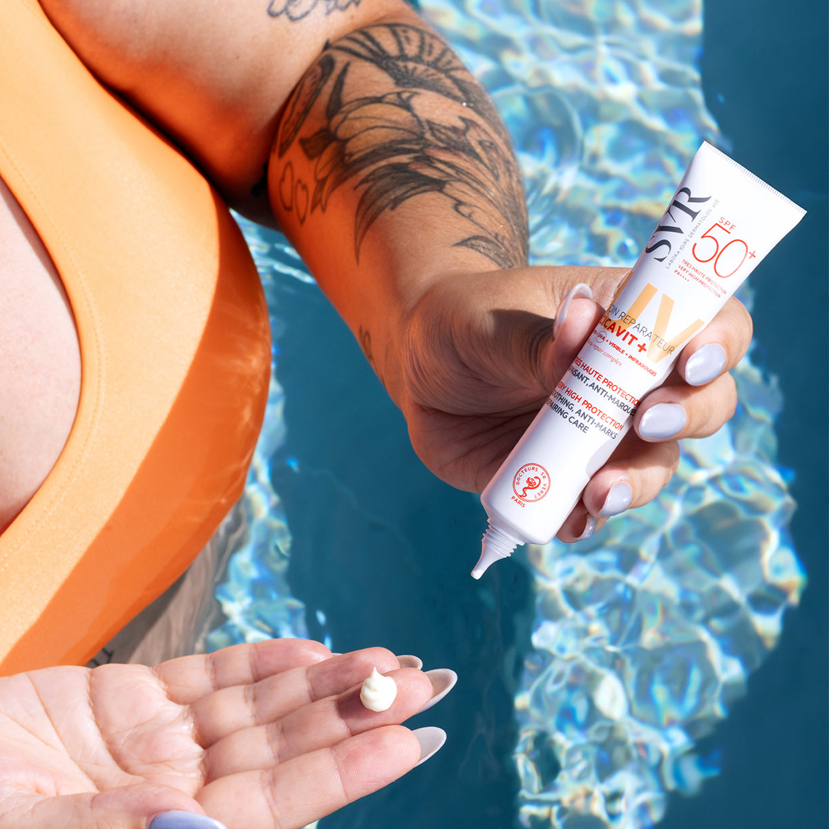 Tube de crème SVR Cicavit+ SPF50+ tenu au-dessus d'une piscine, montrant une noisette de crème sur la paume de la main.