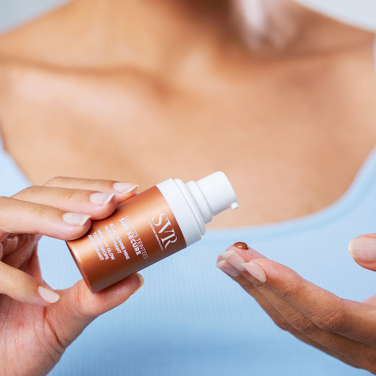 SVR SUN SECURE Gouttes Teintées bronze bottle with pump, dispensing a drop of tinted antioxidant serum onto a finger.