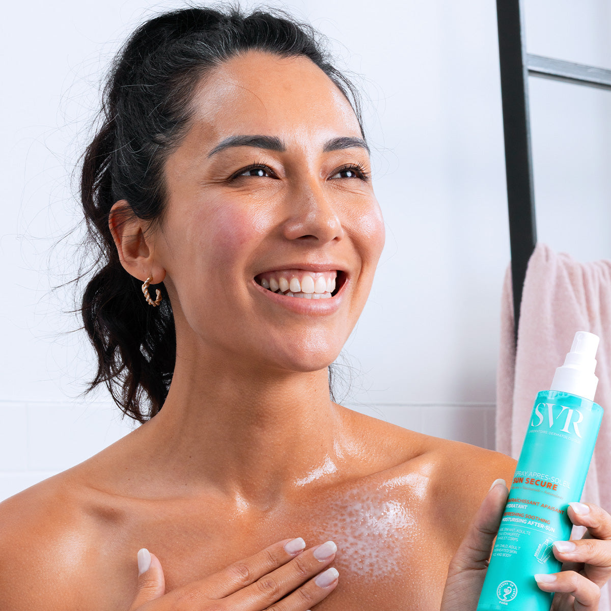 Femme souriante appliquant le spray après-soleil SVR Sun Secure turquoise sur sa peau hydratée après l'exposition au soleil.