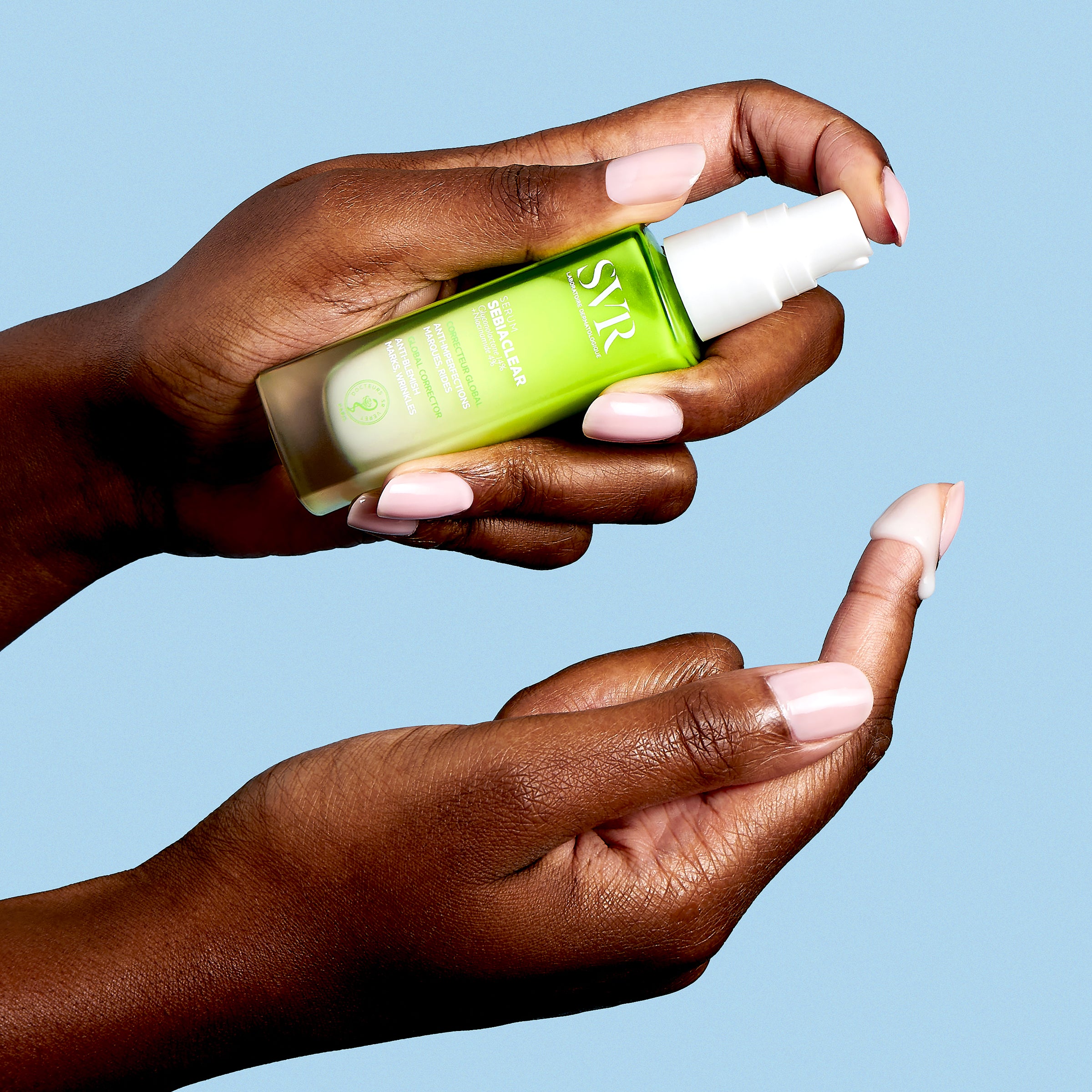 Hands holding a green SVR Sebiaclear serum bottle with a white pump, dispensing a drop of white cream onto a fingertip.