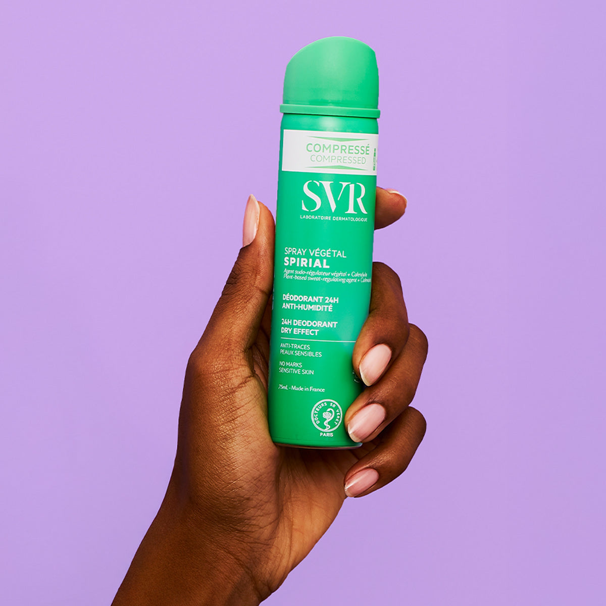 Main tenant un spray déodorant SVR Spirial Végétal vert compressé de 75ml sur fond violet.